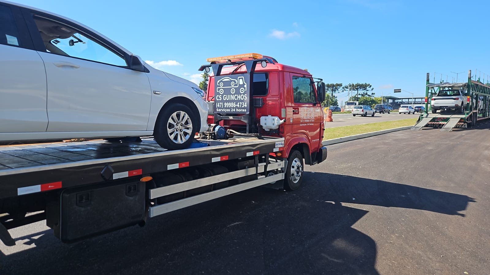 Caminhão plataforma vermelho da CS Guinchos transportando um carro em dia claro